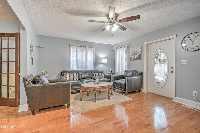 living room featuring ceiling fan, a textured ceiling, and light wood-type flooring