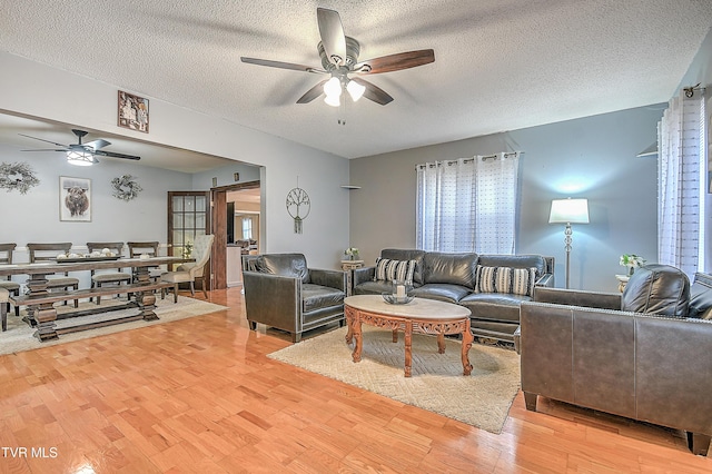 living room with ceiling fan, a textured ceiling, and light hardwood / wood-style floors