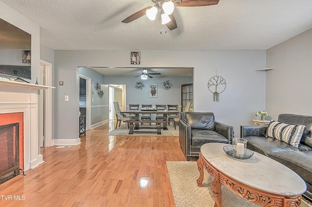 living room with ceiling fan, a textured ceiling, and light wood-type flooring