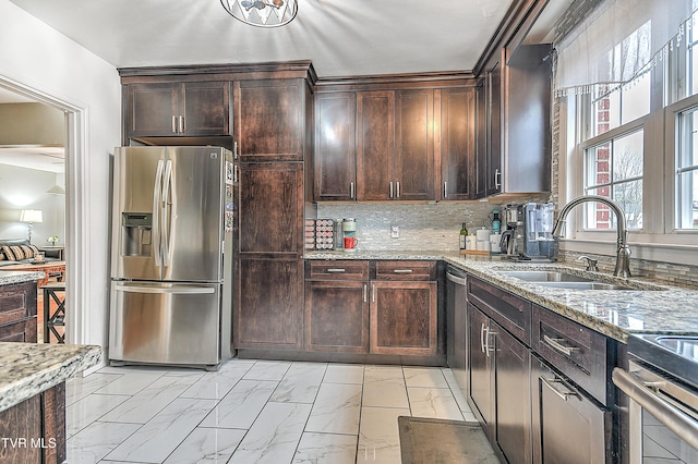 kitchen with dark brown cabinetry, sink, light stone countertops, and appliances with stainless steel finishes