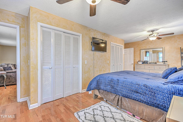 bedroom with multiple closets, ceiling fan, light hardwood / wood-style floors, and a textured ceiling