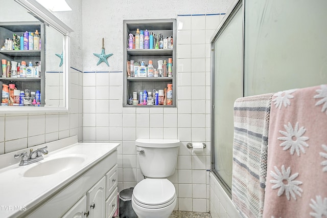 full bathroom featuring vanity, tile walls, bath / shower combo with glass door, and toilet