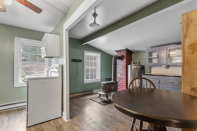 dining space featuring a wood stove, a baseboard heating unit, lofted ceiling with beams, washer / clothes dryer, and light wood-type flooring