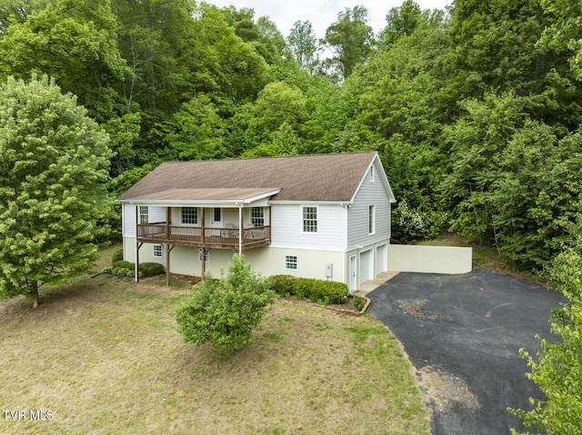 view of front of house with aphalt driveway, a deck, roof with shingles, an attached garage, and a forest view