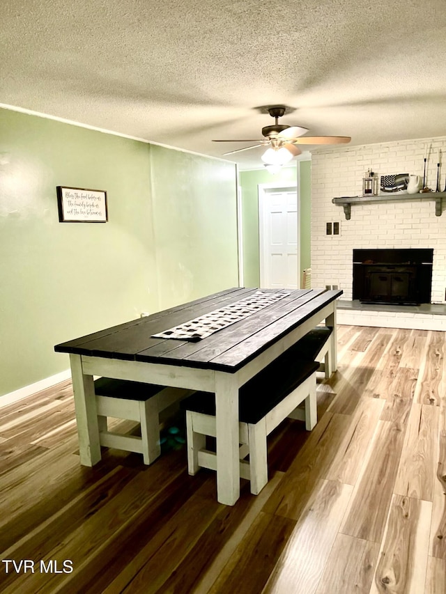 unfurnished dining area with ceiling fan, hardwood / wood-style floors, a textured ceiling, and a fireplace