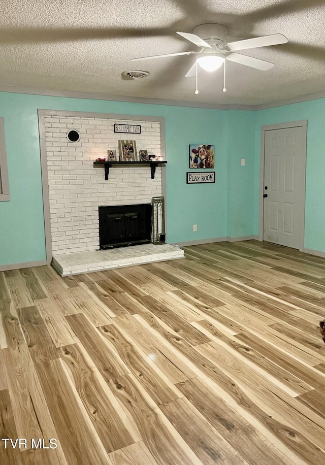 unfurnished living room with ceiling fan, hardwood / wood-style floors, a brick fireplace, and a textured ceiling