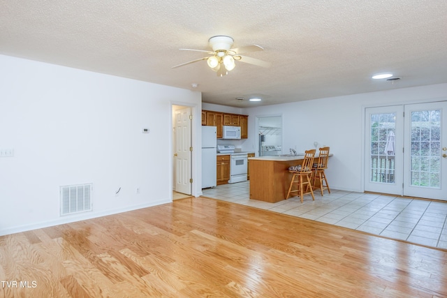 kitchen with sink, white appliances, light hardwood / wood-style flooring, a kitchen breakfast bar, and a textured ceiling