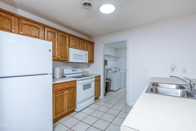 kitchen featuring sink, light tile patterned floors, washing machine and clothes dryer, and white appliances