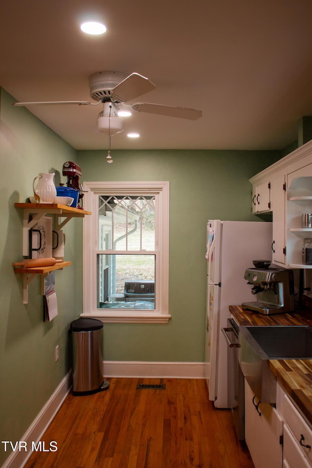 kitchen with ceiling fan, butcher block counters, hardwood / wood-style floors, white cabinets, and white fridge