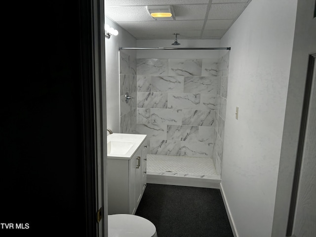 bathroom featuring tiled shower, vanity, toilet, and a paneled ceiling