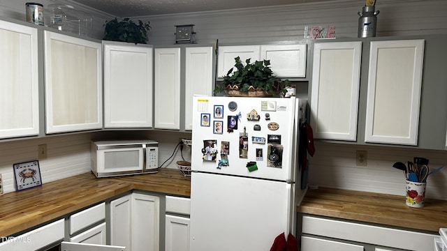 kitchen with white cabinets, crown molding, wooden counters, and white appliances