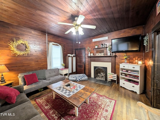 living room with wood-type flooring, wooden ceiling, ceiling fan, and wood walls