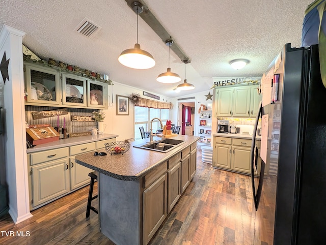 kitchen with a kitchen bar, sink, a center island with sink, black refrigerator, and dark hardwood / wood-style flooring