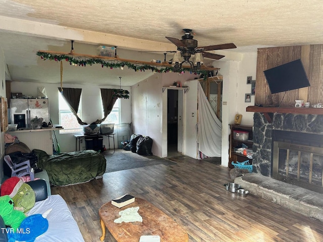 living room with a stone fireplace, wood-type flooring, ceiling fan, a textured ceiling, and beam ceiling