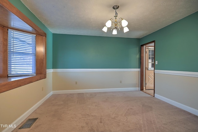 carpeted spare room featuring a textured ceiling and a chandelier