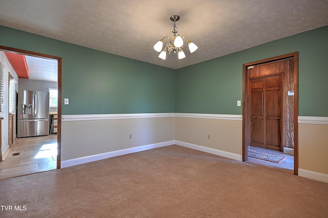 unfurnished room with an inviting chandelier, light carpet, and a textured ceiling