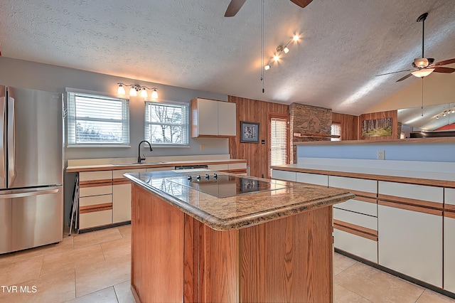 kitchen with sink, stainless steel fridge, white cabinetry, a kitchen island, and black electric cooktop