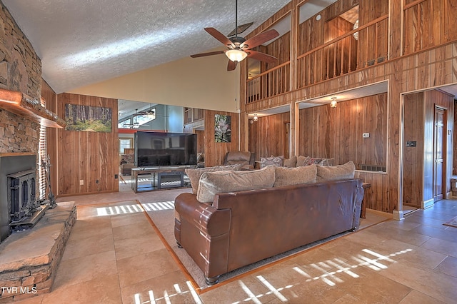 living room with ceiling fan, wooden walls, high vaulted ceiling, and a textured ceiling