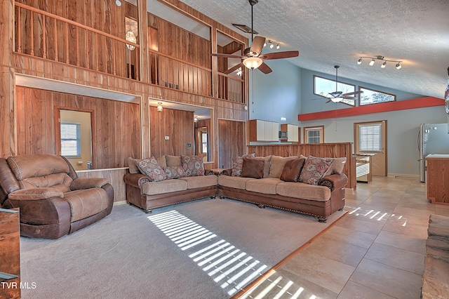 tiled living room featuring ceiling fan, high vaulted ceiling, a textured ceiling, and wood walls