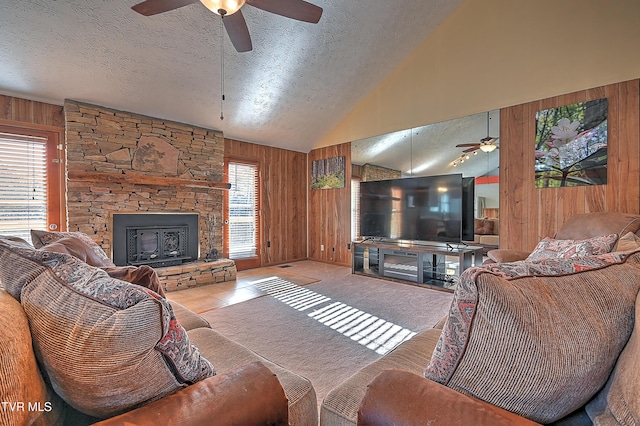 carpeted living room featuring ceiling fan, wooden walls, high vaulted ceiling, a fireplace, and a textured ceiling