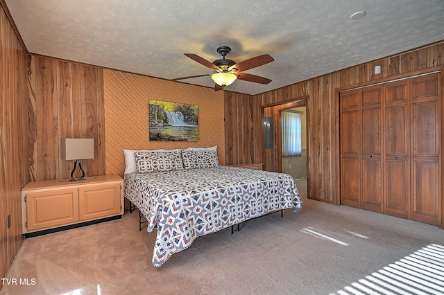 carpeted bedroom with ceiling fan, wooden walls, a textured ceiling, and a closet