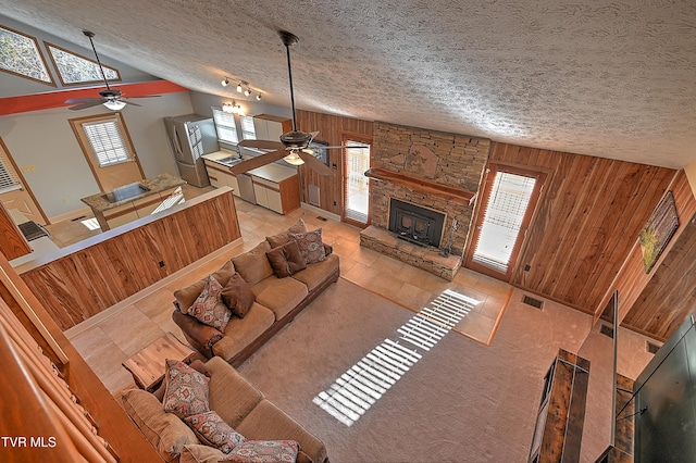 unfurnished living room featuring lofted ceiling, a stone fireplace, wood walls, a textured ceiling, and ceiling fan