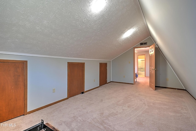 bonus room with lofted ceiling, light colored carpet, and a textured ceiling