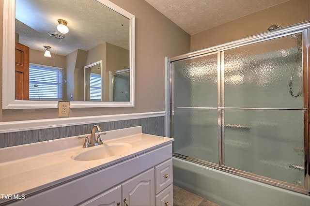 bathroom featuring vanity, combined bath / shower with glass door, and a textured ceiling