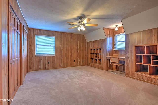 unfurnished living room with ceiling fan, light colored carpet, a textured ceiling, and wooden walls