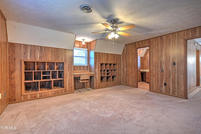 unfurnished living room featuring light colored carpet, a textured ceiling, and wood walls