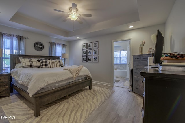 bedroom featuring ceiling fan, connected bathroom, a raised ceiling, and light hardwood / wood-style floors