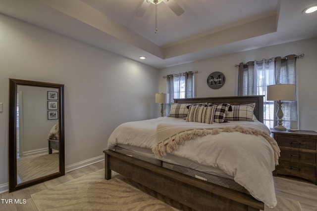 bedroom featuring a raised ceiling, ceiling fan, and light hardwood / wood-style flooring