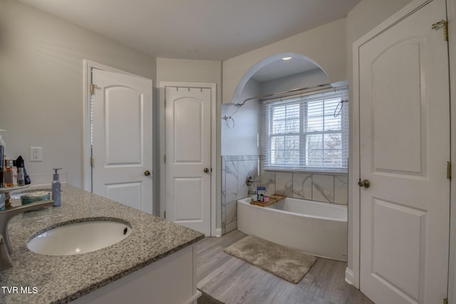 bathroom with hardwood / wood-style flooring, a bathing tub, tile walls, and vanity