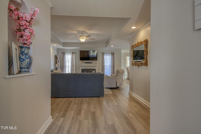 unfurnished living room with crown molding, ceiling fan, a raised ceiling, and light hardwood / wood-style floors