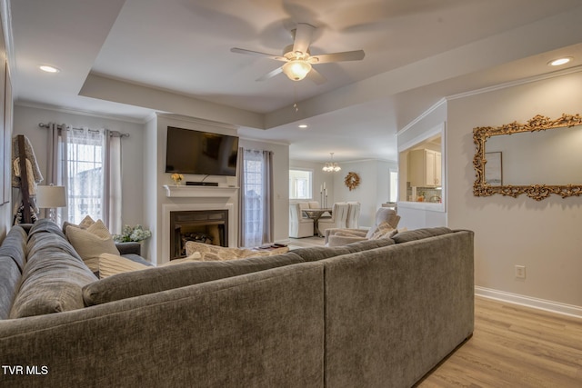 living room featuring a raised ceiling, ornamental molding, ceiling fan, and light hardwood / wood-style flooring