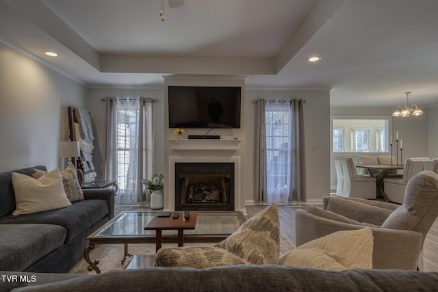 living room featuring a raised ceiling, ornamental molding, plenty of natural light, and an inviting chandelier