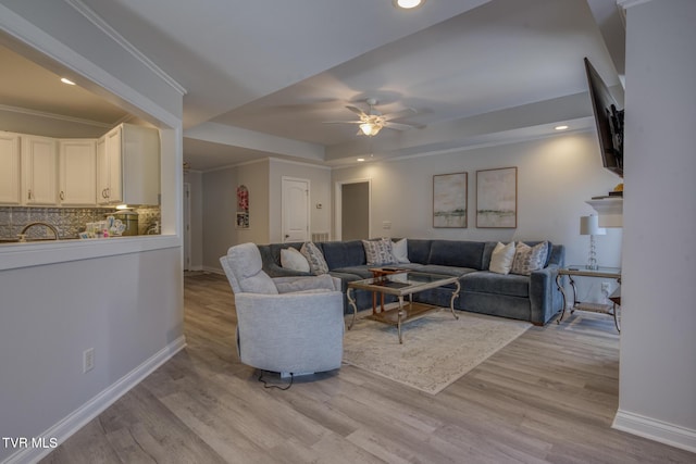 living room with crown molding, ceiling fan, a raised ceiling, and light wood-type flooring