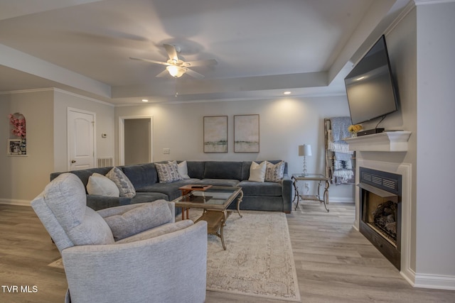 living room with a raised ceiling, ceiling fan, crown molding, and light hardwood / wood-style floors