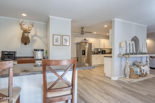 kitchen with crown molding, stainless steel refrigerator with ice dispenser, light hardwood / wood-style floors, white cabinets, and decorative backsplash