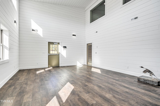 unfurnished living room with wood walls, dark hardwood / wood-style flooring, and a high ceiling