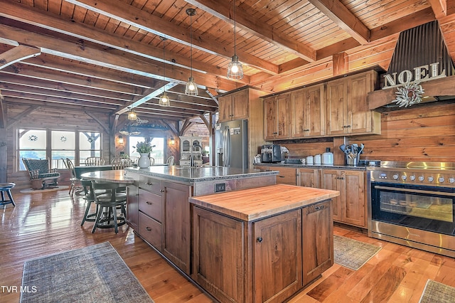 kitchen featuring hardwood / wood-style flooring, stainless steel appliances, wood walls, and a center island with sink