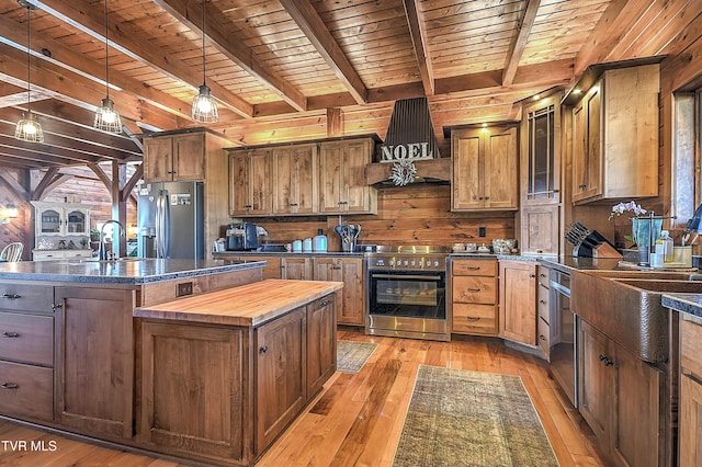 kitchen with stainless steel appliances, premium range hood, a kitchen island with sink, and wood walls