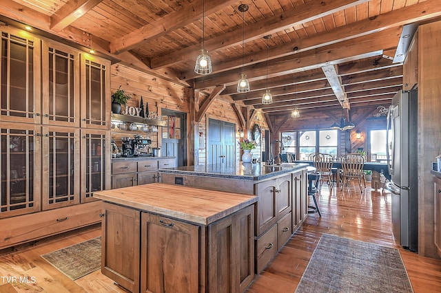 kitchen with stainless steel refrigerator, butcher block counters, hanging light fixtures, hardwood / wood-style floors, and a center island with sink