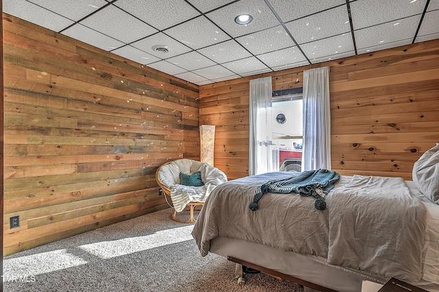 carpeted bedroom featuring wooden walls and a drop ceiling