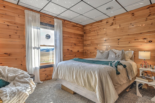 bedroom with a drop ceiling, carpet floors, and wood walls