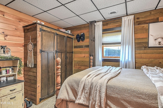 bedroom featuring wooden walls, light colored carpet, a barn door, and a paneled ceiling