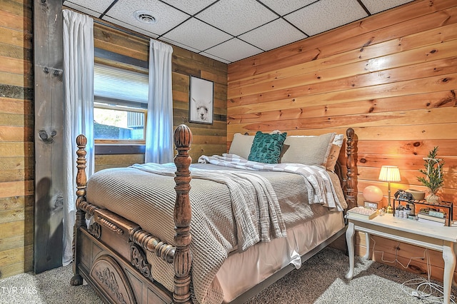 carpeted bedroom featuring a paneled ceiling and wood walls