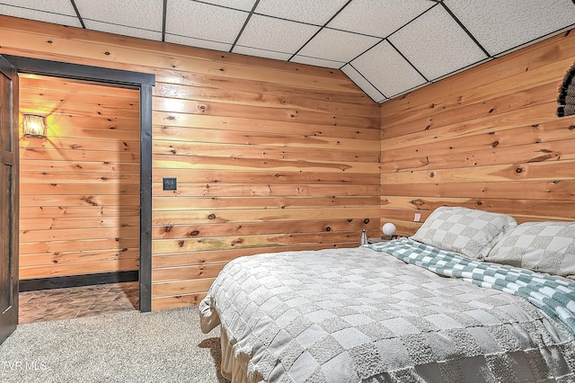 bedroom featuring a drop ceiling, carpet, and wood walls