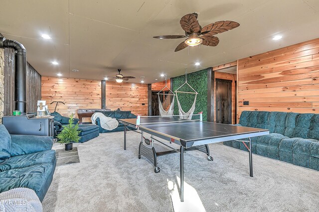 game room featuring ceiling fan, wooden walls, carpet, and a wood stove