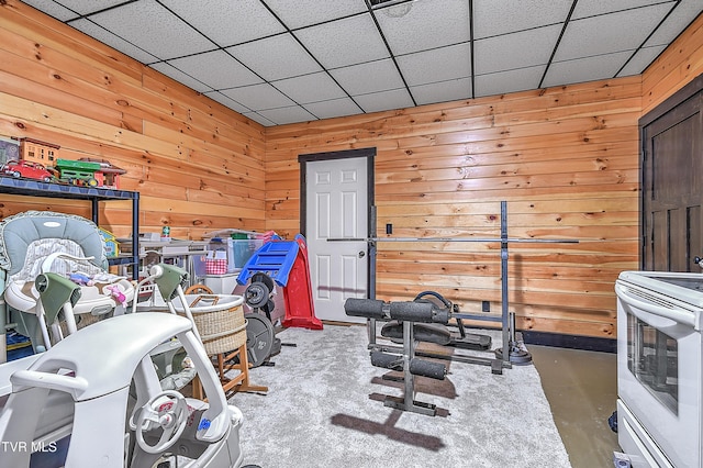 exercise area featuring wood walls and a drop ceiling